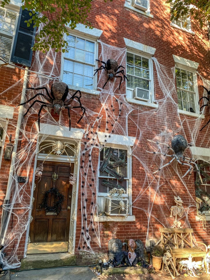Porte avant et façade d’une maison en briques rouge, accessoires d’Halloween incluant des toiles d’araignée et des araignées géantes 