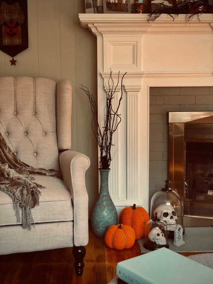 Vue d’un salon incluant un fauteuil, un vase, un foyer, des globes contenant des têtes de mort et deux citrouilles en tissu posées sur le sol