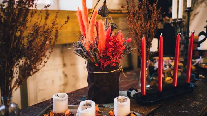Table automnale incluant des chandelles de couleur blanche et de couleur rouge, un vase garni de fleurs séchées et un chandelier noir