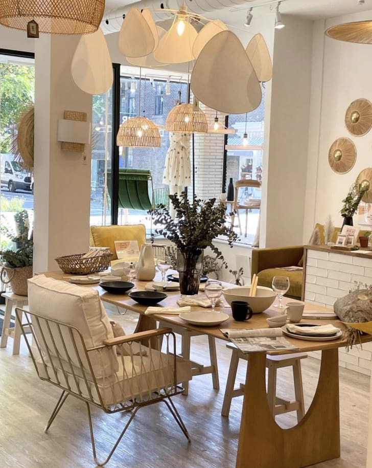 Vue sur la boutique Coeur d'artichaut, incluant une table de cuisine et de la vaisselle, des fleurs séchés, un fauteuil blanc, et différents types de luminaires suspendus