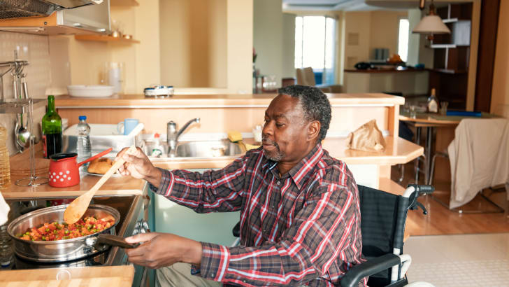 Homme âgé dans un fauteuil roulant qui fait de la nourriture sur une cuisinière
