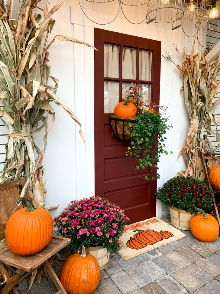 Porte d'entrée décorée pour l'automne incluant un tapis, des chrysantèmes, des citrouilles orange et des branches séchées