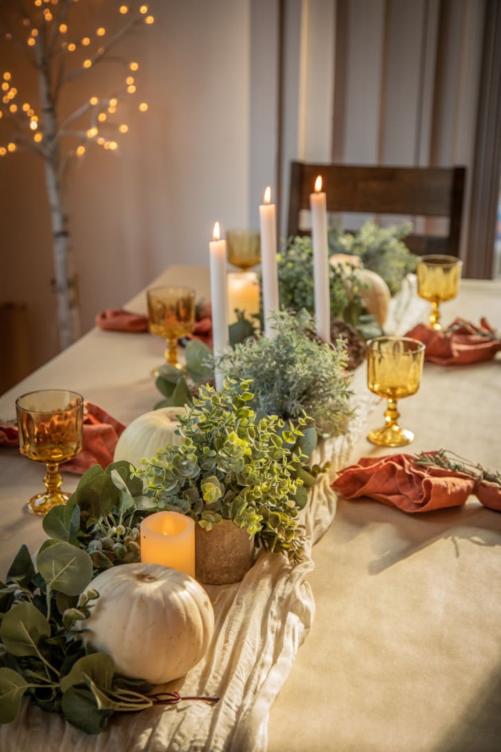 Table décorée pour l'automne avec verres translucides, bougies, citrouilles blanches, chemin de table en lin et feuillages