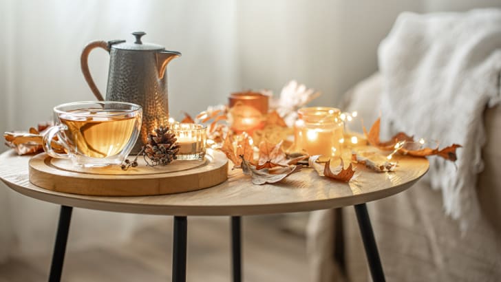 Idées de décoration d'automne avec du thé, des feuilles sèches et des bougies allumées sur un fond flou, guirlandes lumineuses posées sur la table