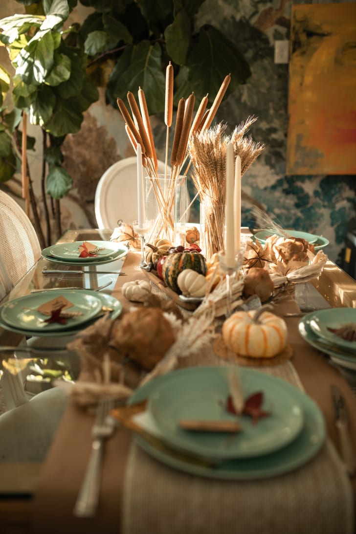 Table automnale avec assiettes bleues, petites citrouilles, tiges de fleurs séchées, chemin de table, ustensiles et bougies blanches