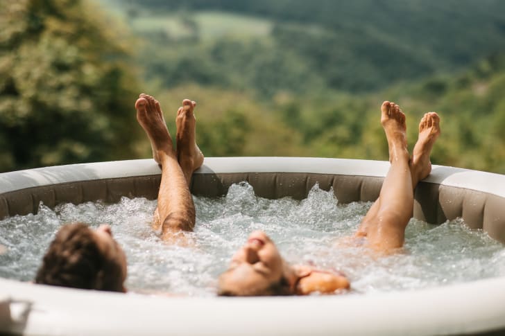 Two people enjoying the benefits of an inflatable whirlpool bath overlooking a mountain forest