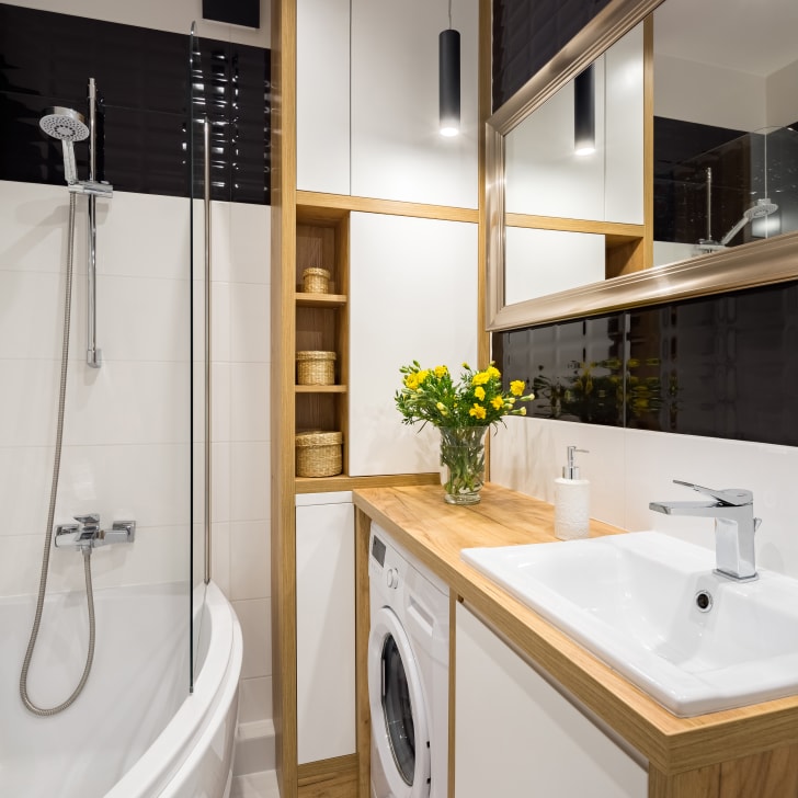 Black and white bathroom with built-in cabinets, shower, vanity and small washing machine