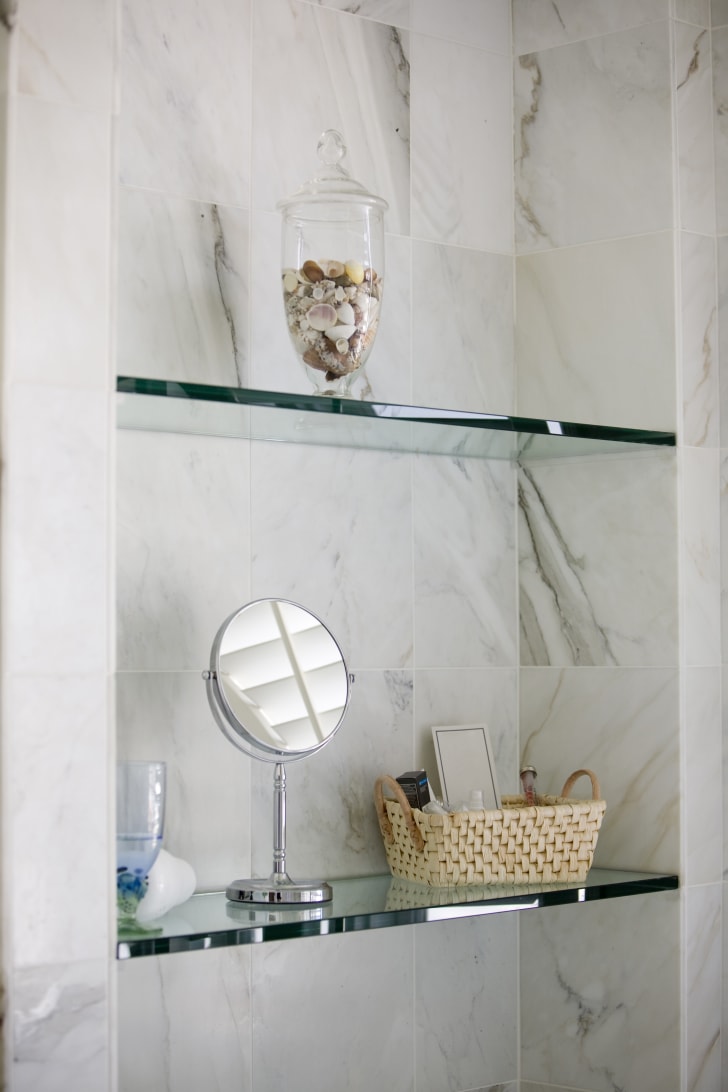 Close-up of glass and marble bathroom shelves with accessories: mirror, basket and potpourri
