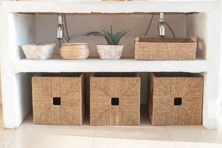 View of the underside of a washbasin, including wicker storage baskets and a faux plant