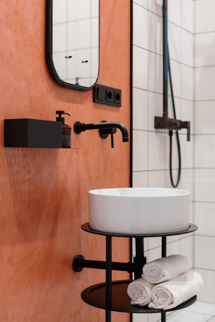 Black bathroom faucets on orange wall and white shower tiles