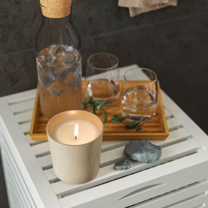 Decorative wooden tray placed on a piece of furniture, accompanied by a candle and small rocks