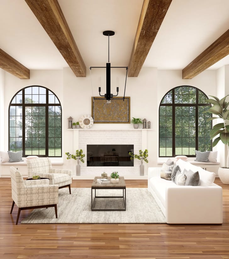 Salon de style farmhouse avec poutres en bois au plafond, un foyer en briques blanches, des fauteuils et un divan dans les teintes de beige, un luminaire et de grandes fenêtres