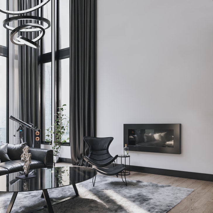 Salon industriel moderne avec de hauts plafonds, des fenêtres industrielles, un canapé en cuir noir, une chaise et une table en métal, devant un haut mur en plâtre avec foyer