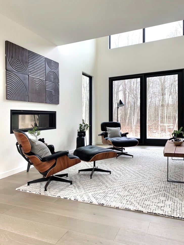 Salon moderne avec fauteuils noir et brun, tableau abstrait noir, tapis, grandes fenêtres et table basse en bois