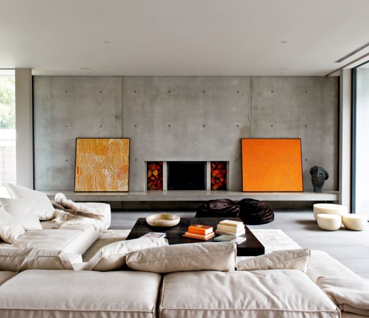 Salon avec mur de béton, cadres de couleur orange et gros divan beige