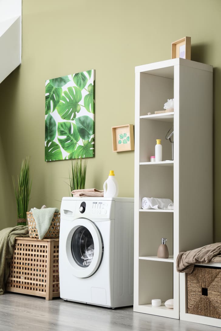 Laundry room with modern washing machine, colored wall, storage shelves and decorations    