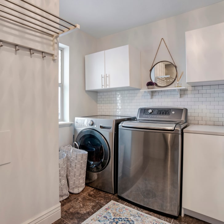 Laundry room with cupboards containing washing machine and dryer, mirror and white ceramic backsplash