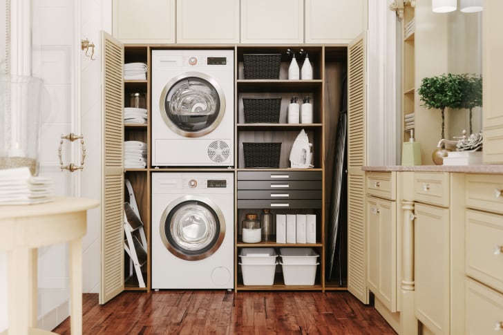 Interior of a modern laundry room with washer and dryer stacked in a cabinet containing shelves and accessories