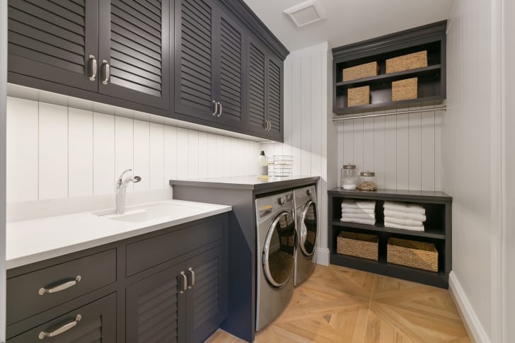 Front-loading appliances with counter space above, in a renovated laundry room with cabinets, shelves and storage baskets
