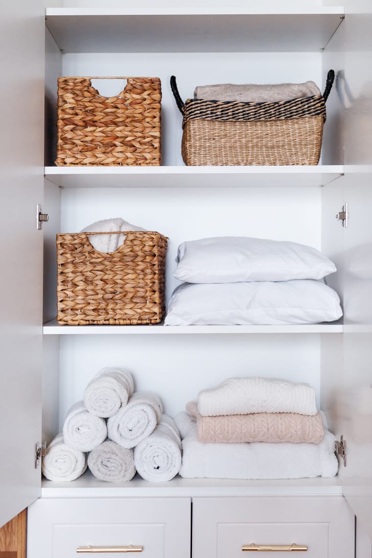 Towels, clothes and pillows organized and folded in wicker baskets on the shelves of a white wardrobe