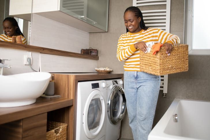 Person in a laundry room set up in a bathroom, with a line basket in their hands
