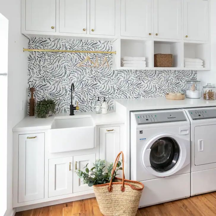 Laundry room with plank cabinets, appliances, wicker basket, sink and designer wallpaper