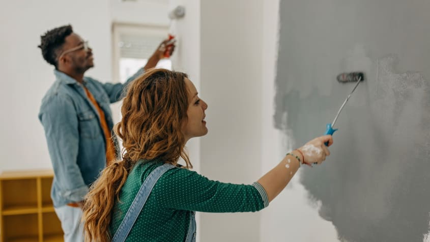 A man and a woman painting a wall gray