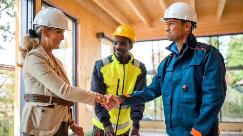 Woman wearing a hard hat shakes hands with a contractor