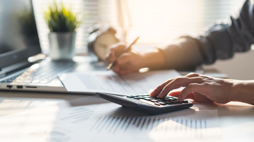 Personne qui utilise une calculatrice et un ordinateur portable pour effectuer des calculs liés à l’achat d’une propriété et à la taxe de bienvenue
