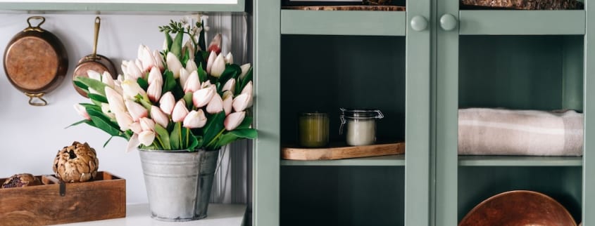 A cabinet with glass doors is painted with the colour sage and houses several decorative accessories