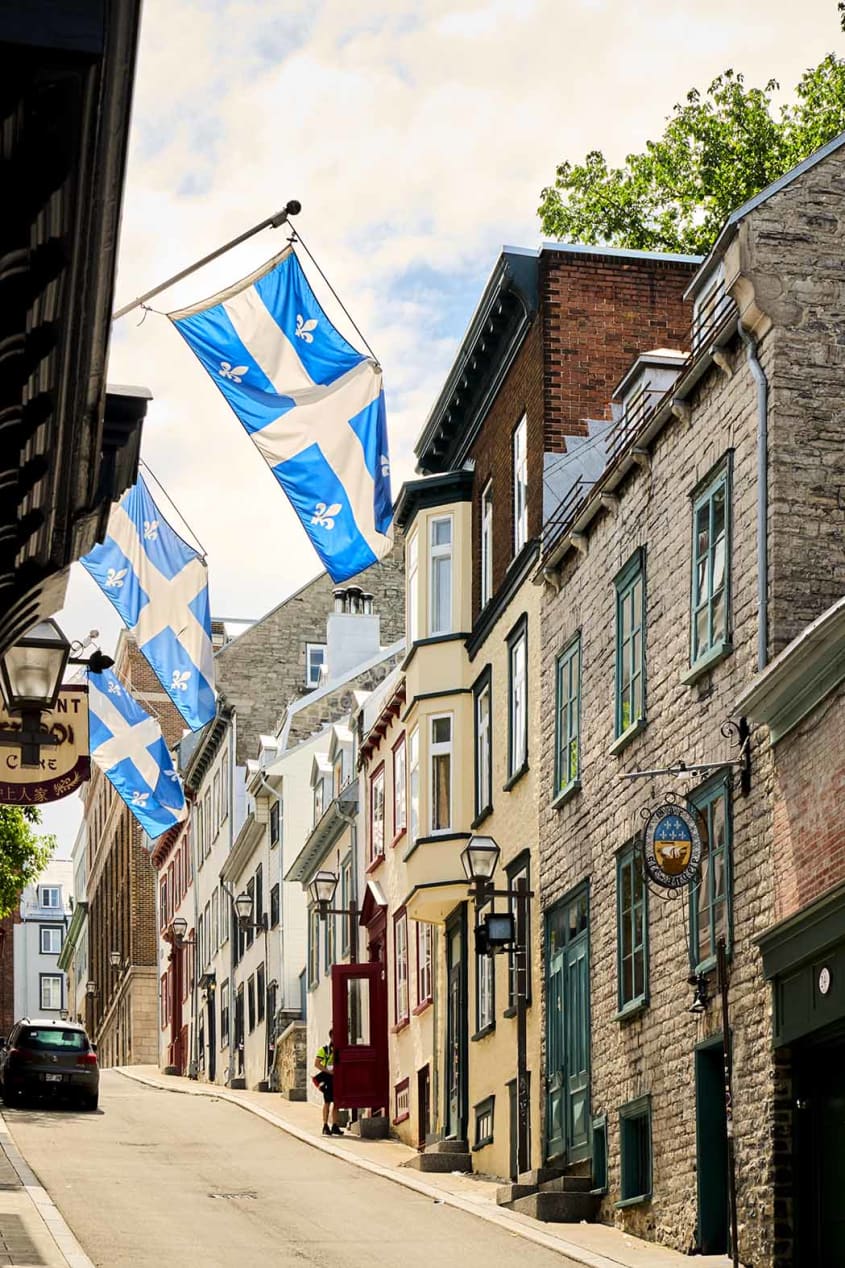 Sloping street in Old Québec with Québec provincial flags and rowhouses