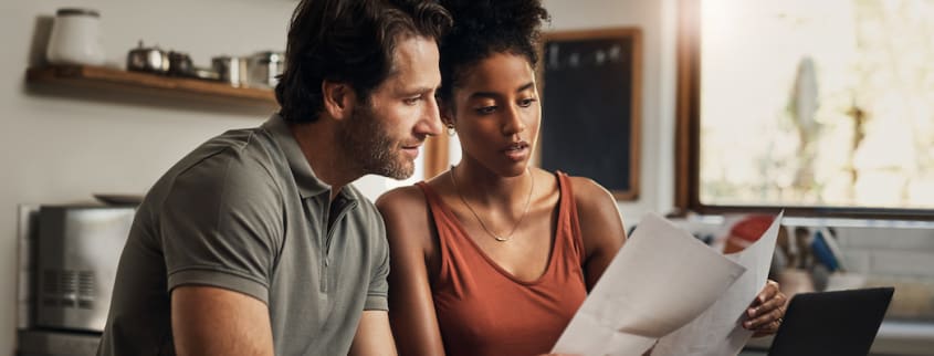 A man and a woman looking at some paperwork in their kitchen