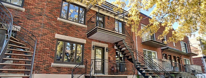 Facade of a red brick duplex with a tree in fall colors