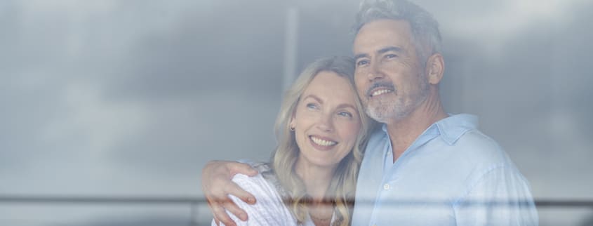 Couple heureux regardant par la fenêtre de sa maison