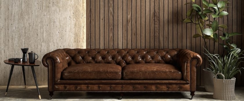 Interior with wood-panelled wall, brown sofa, backlighting, small coffee table and plant
