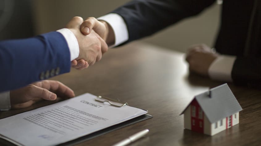 Poignée de main entre courtier immobilier et client au-dessus d'un contrat