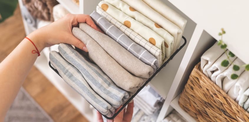 Main qui fait du rangement en plaçant des linges et des draps dans un tiroir