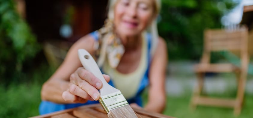Femme qui applique une couche de peinture sur un mobilier de jardin dans sa cour