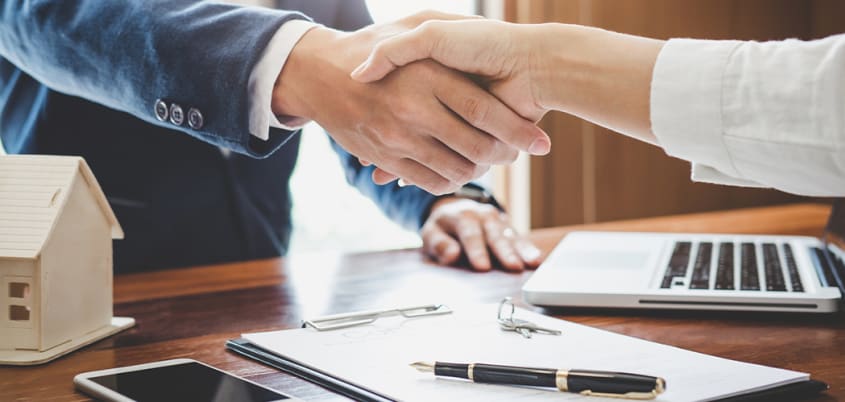 Buyer's broker and client shaking hands over a brokerage contract for buying a house