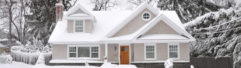 Une maison de banlieue grise située sur un grand terrain est couverte de neige