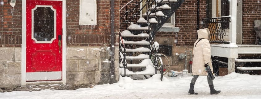 A woman walks on a snow-covered Montreal street in front of a typical apartment building with spiral staircase.
