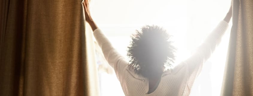 Femme ouvrant les rideaux pour faire entrer le soleil
